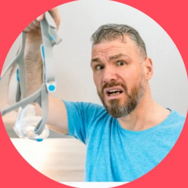 Frustrated man holding up a CPAP mask and hose