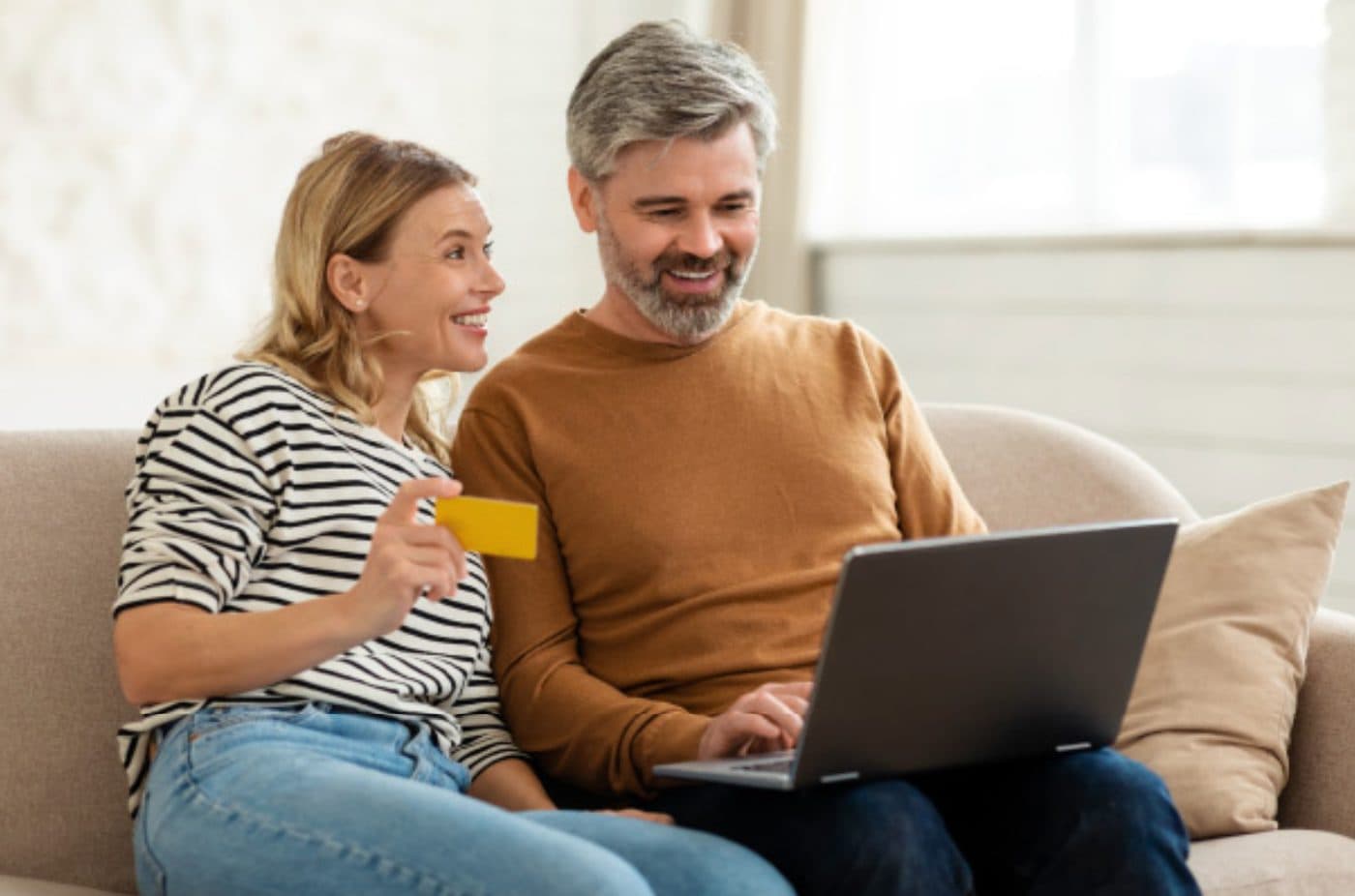 Couple on the couch paying online with a card and laptop