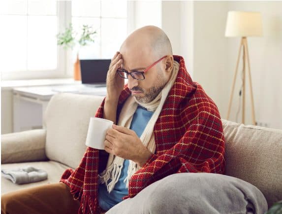 Man wrapped in a blanket on the couch, unwell with allergies