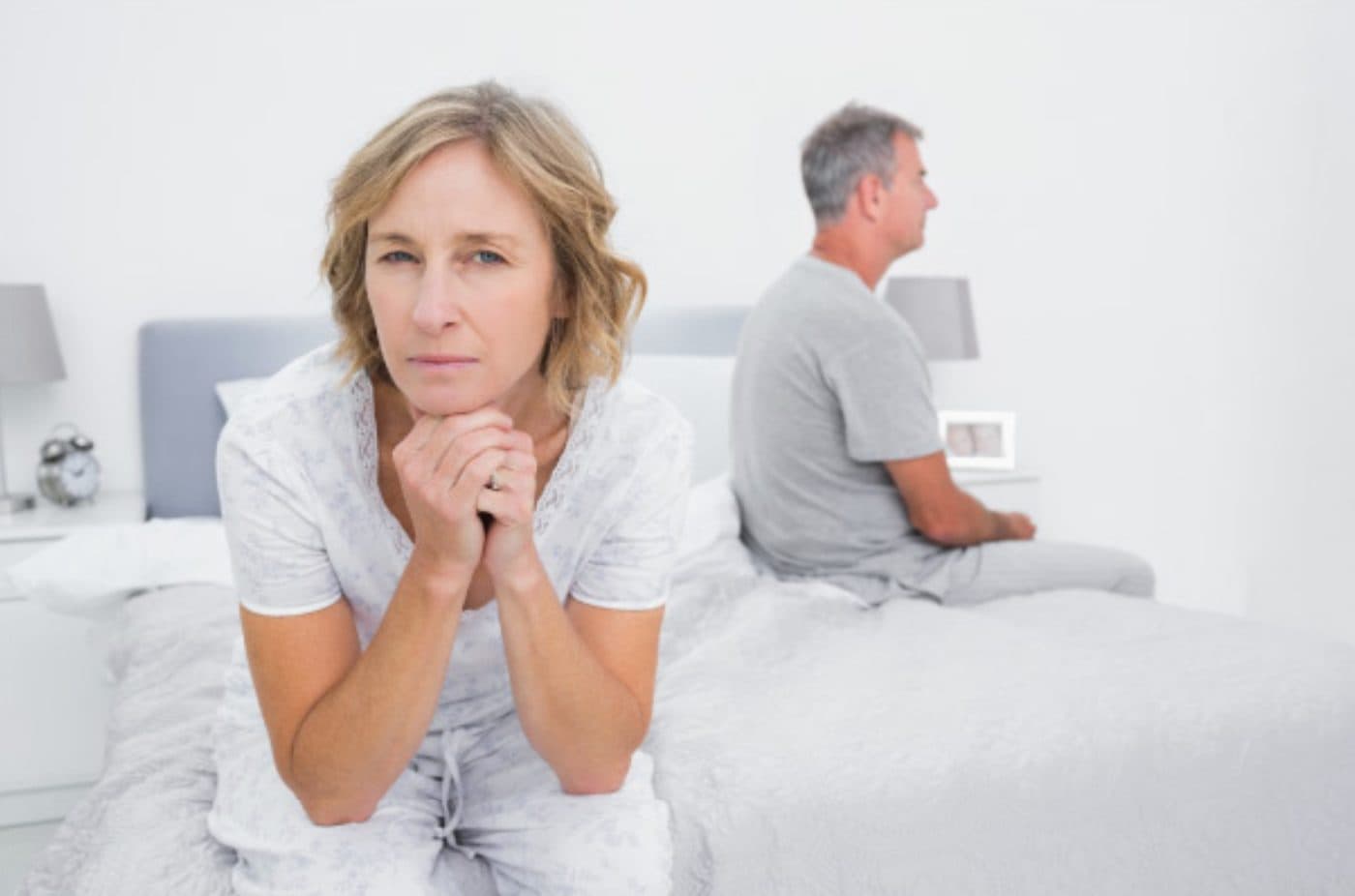 Tired woman sitting on the bed with her partner behind her